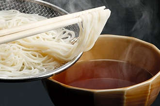 温かい汁の入った椀の中に茹で上がったそうめんを注いでいる写真