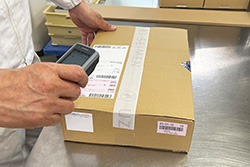 外箱に貼られたバーコードリーダーを読み取っている様子の写真