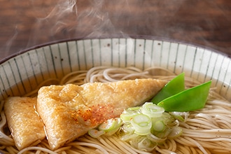 どんぶりの中にあたたかいつゆでお蕎麦と油揚げやネギなどをトッピングした写真