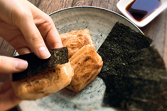 タレを絡めた焼きたての餅に海苔を巻いている写真