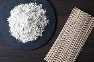 乾麺のそばと皿に盛ったそば粉を並べている写真