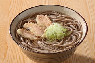 器の中に冷たい肉そばと輪切りのネギと鶏肉を乗せた写真