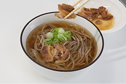 お肉を冷たい肉そばの上にトッピングしている写真