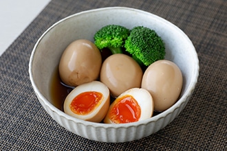 つゆに使って薄く茶色がかった煮卵とブロッコリーを一緒に添えた器の写真